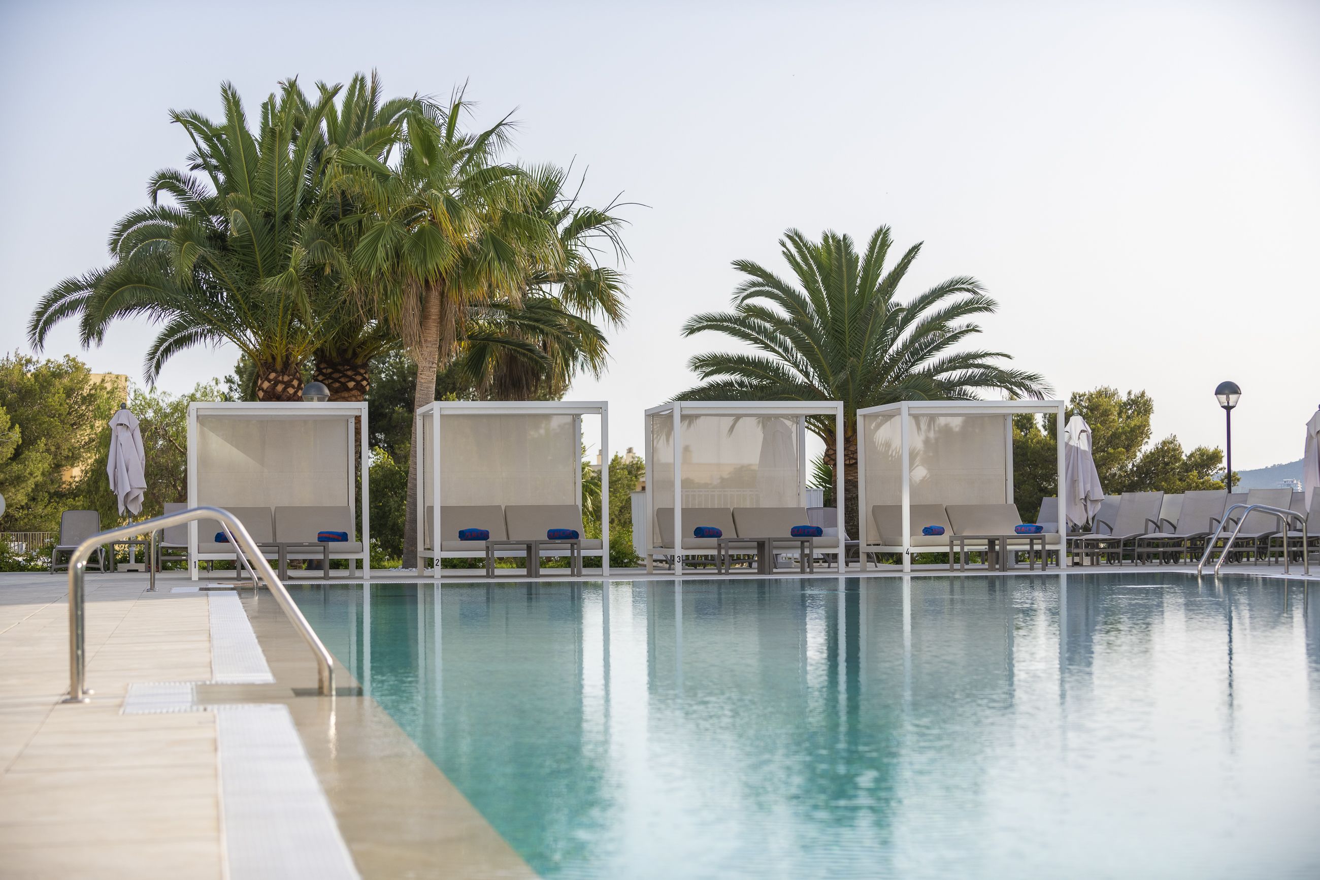 Un área de piscina con sillas de descanso y palmeras.