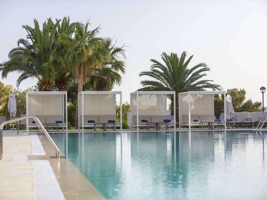 Un área de piscina con sillas de descanso y palmeras.