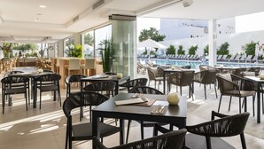A modern dining area with tables and chairs, a poolside view, and a glass partition. - Tomir Portals Suites - Adults Only (+16) (Calvia)