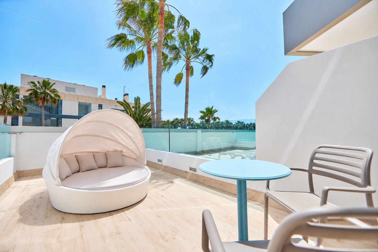 Un espace extérieur moderne aménagé avec une table ronde et des chaises, un coin salon confortable et un point de vue sur les palmiers et les bâtiments.