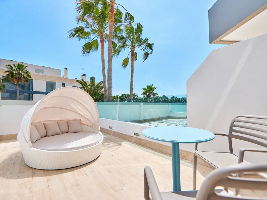 Un espace extérieur moderne aménagé avec une table ronde et des chaises, un coin salon confortable et un point de vue sur les palmiers et les bâtiments.