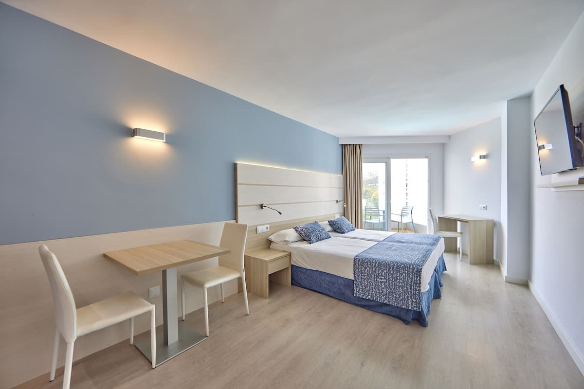 A modern hotel room with a bed, desk, chair, and a TV.