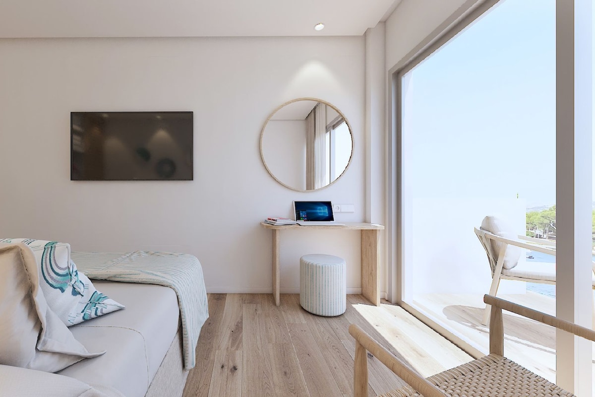 Habitación de hotel moderna con una cama, un escritorio con una computadora portátil, un espejo redondo y vistas al exterior.