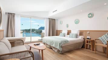 Habitación de hotel con una cama grande, un sofá, una mesita y vista al mar.