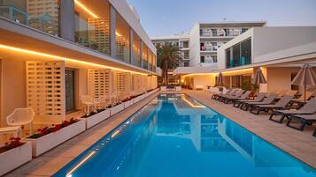 Un hotel moderno con una larga piscina, tumbonas y barandilla de cristal.