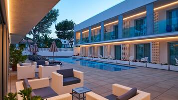 A modern outdoor pool area with lounge chairs and umbrellas, a swimming pool, and a building with large windows and balconies.