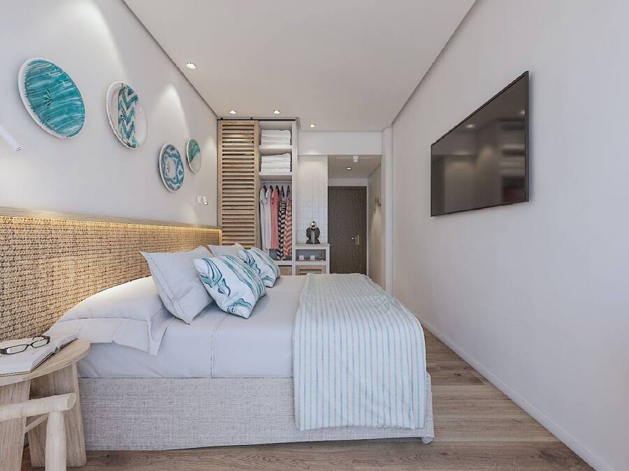A modern bedroom with a woven headboard, a bed with striped bedding, a bedside table with glasses and a book, and a TV mounted on the wall.