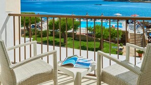 Un balcón con sillas de mimbre, una mesa con revistas y vistas a una piscina y una playa.