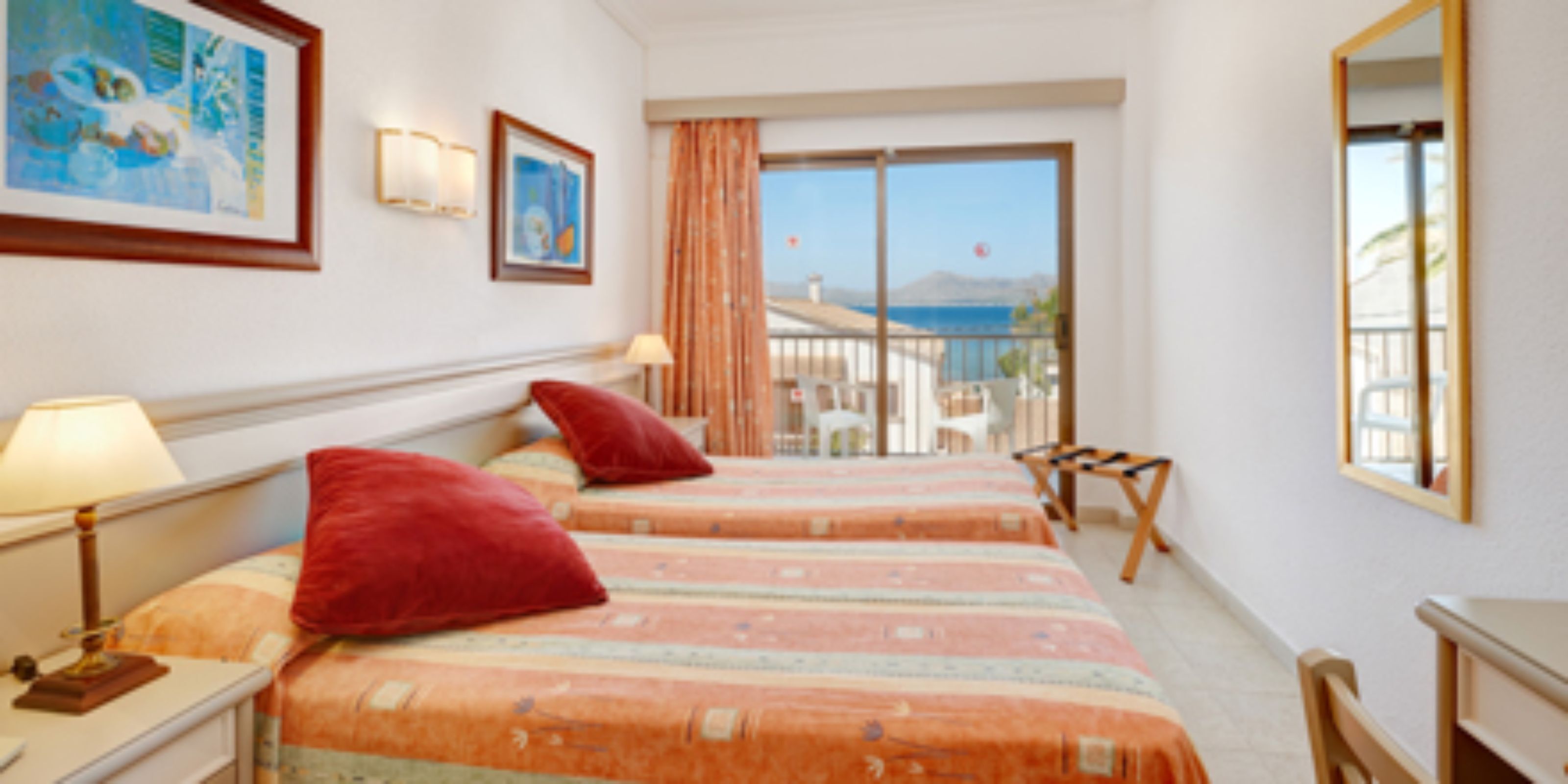 A hotel room with two beds, a balcony with a view, a desk, and a chair.