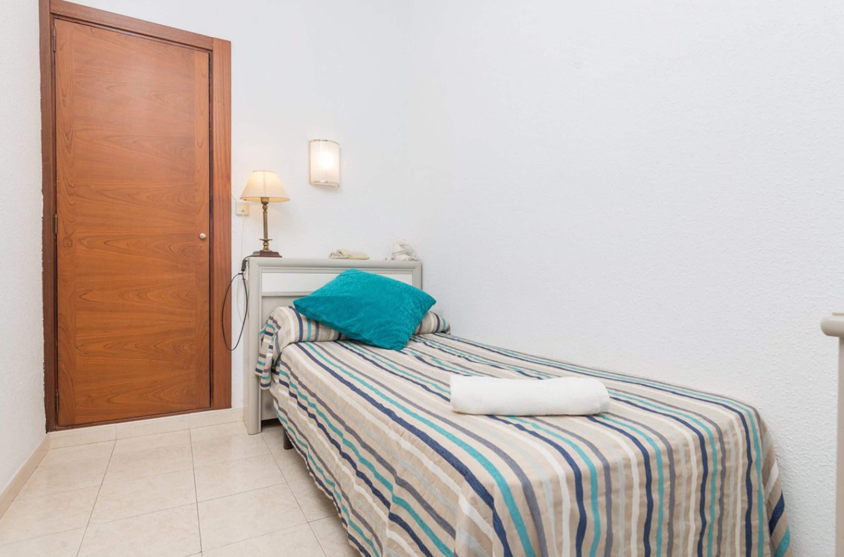 Un dormitorio pequeño y ordenado con una cama individual, una mesita de noche con lámpara y una puerta de madera.