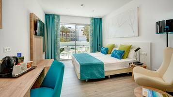 Habitación de hotel con cama, escritorio, silla, televisor y balcón con vistas.