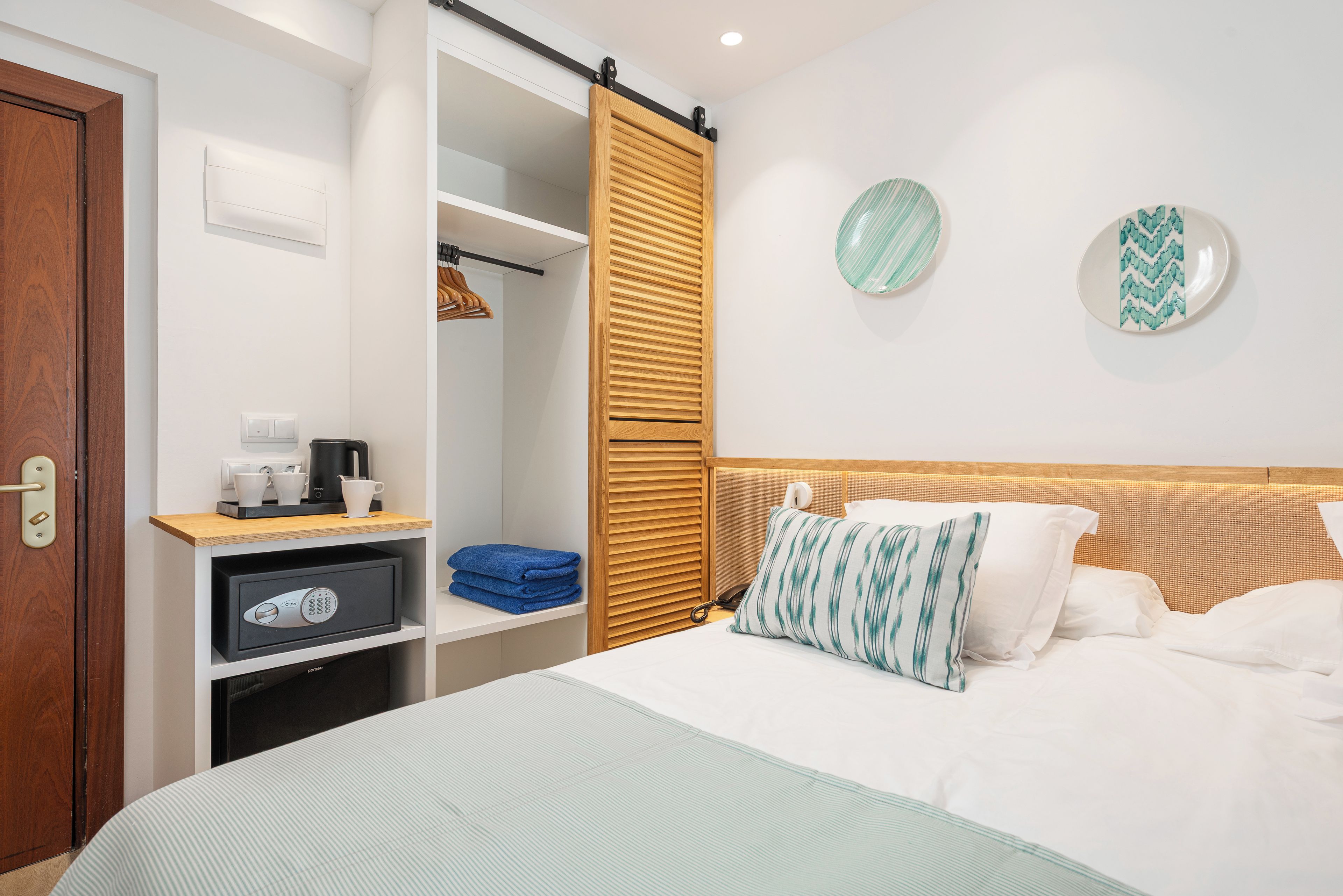 Habitación de hotel con cama, armario, escritorio con cafetera y caja fuerte.