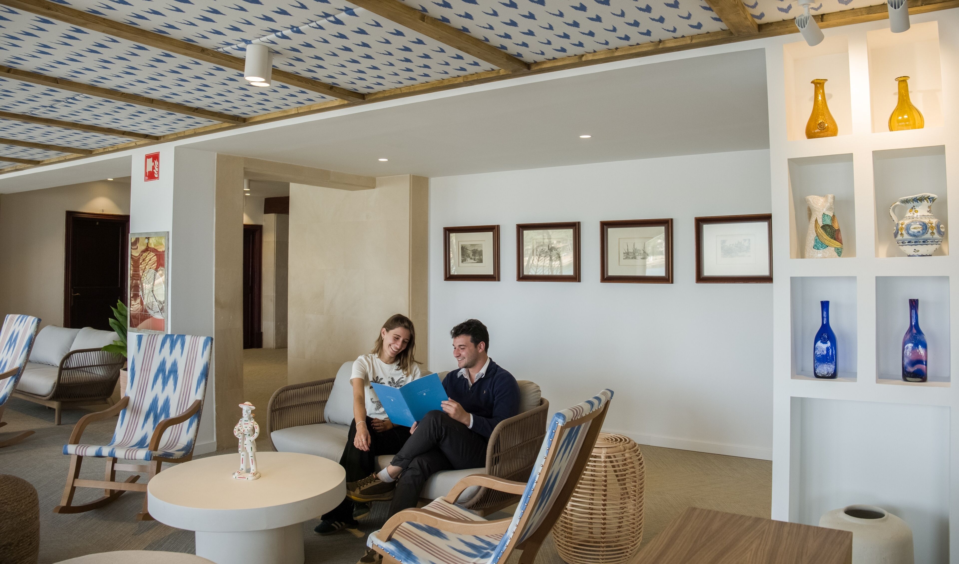 A modern lounge area with wicker furniture, a round table, and wall-mounted shelves with decorative vases.