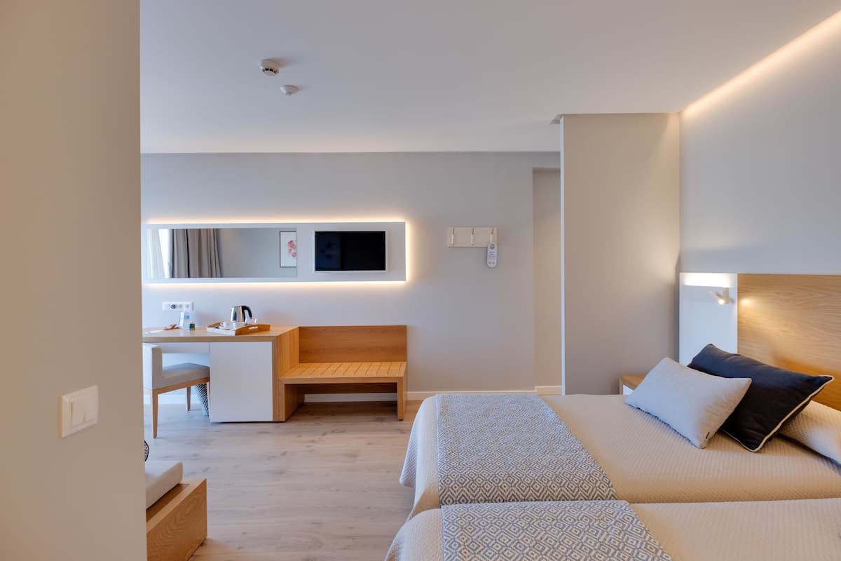 A modern hotel room with a wooden desk, a comfortable chair, a bed with patterned bedding, and a bedside table.