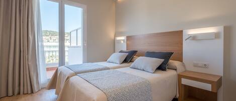 A modern hotel room with two beds, a wooden headboard, bedside tables, and a balcony with a view.