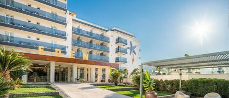A multi-story hotel with a modern design, featuring balconies, a well-maintained garden, and outdoor seating areas.