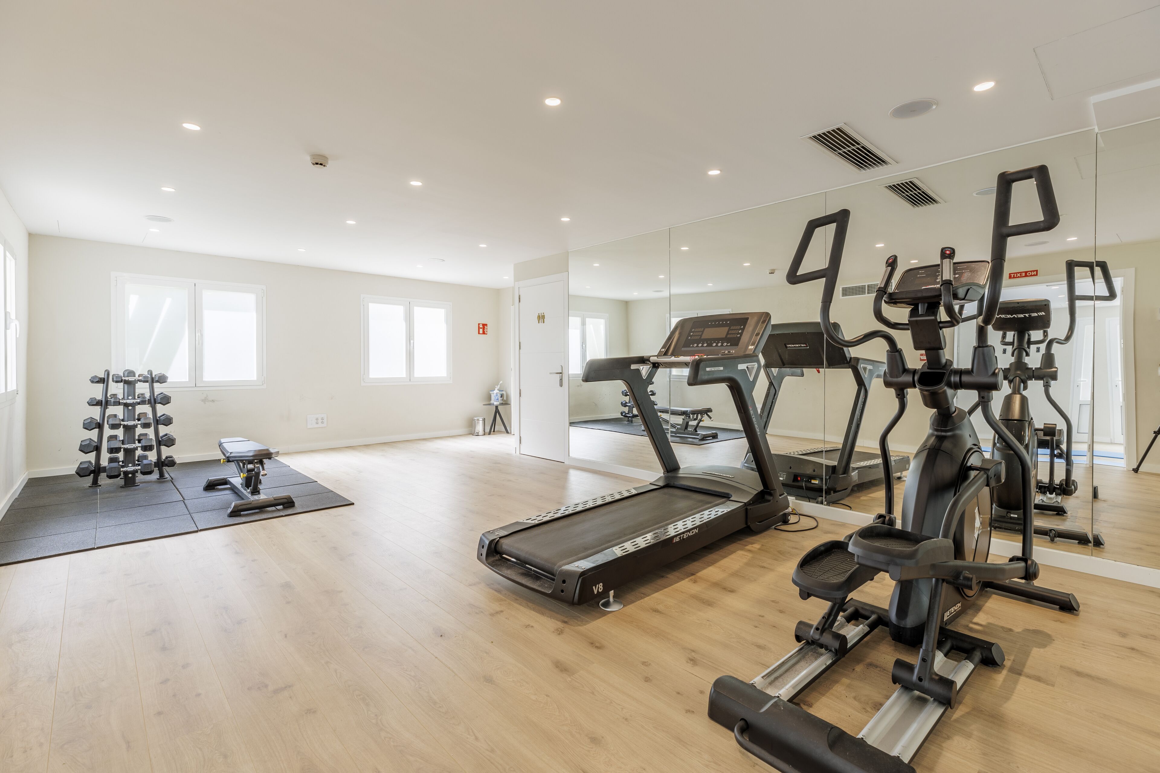 Een ruime fitnessruimte met loopbanden, een gewichtbank en een spiegelwand.