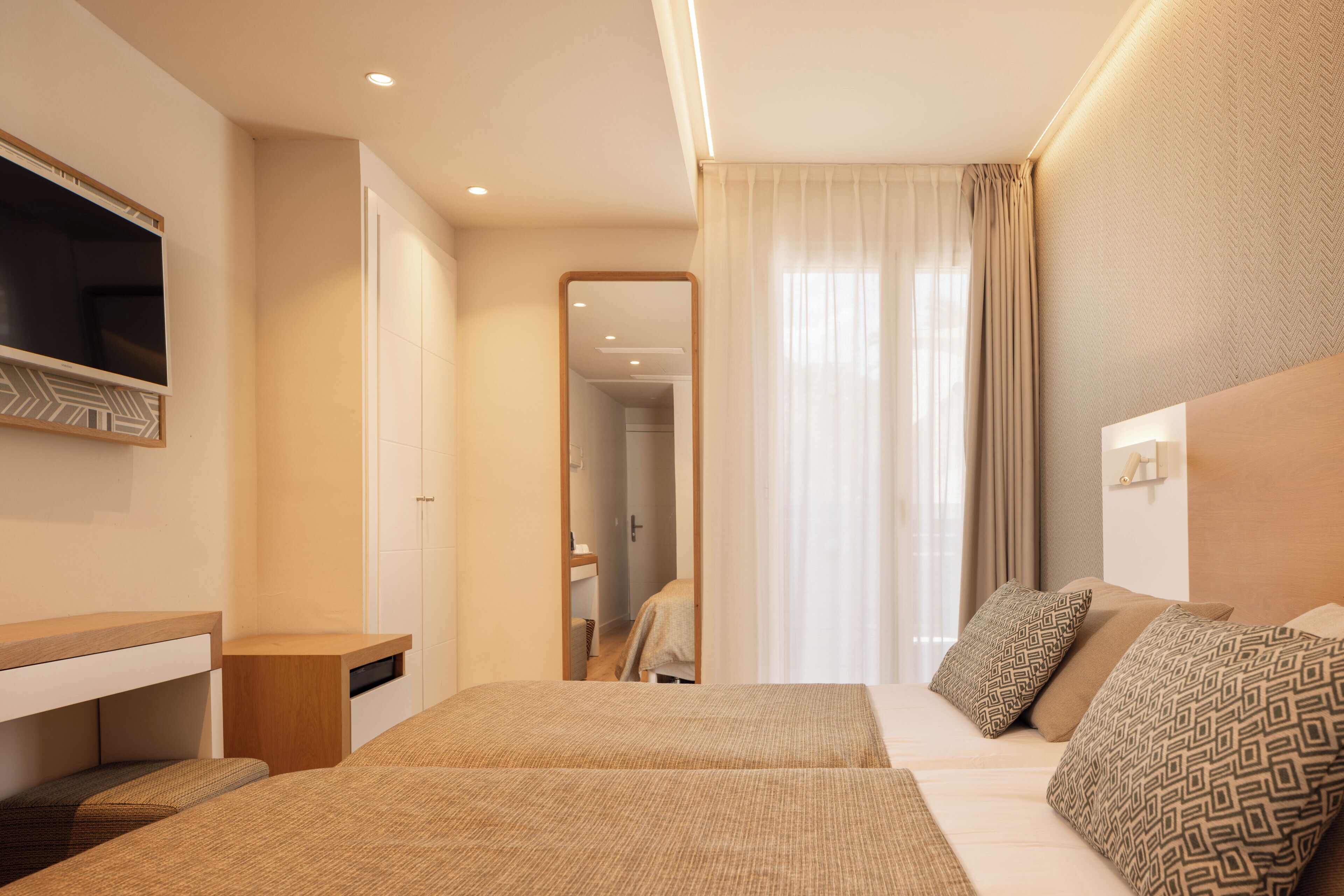 A hotel room with a bed, a TV, a desk, and a mirror.