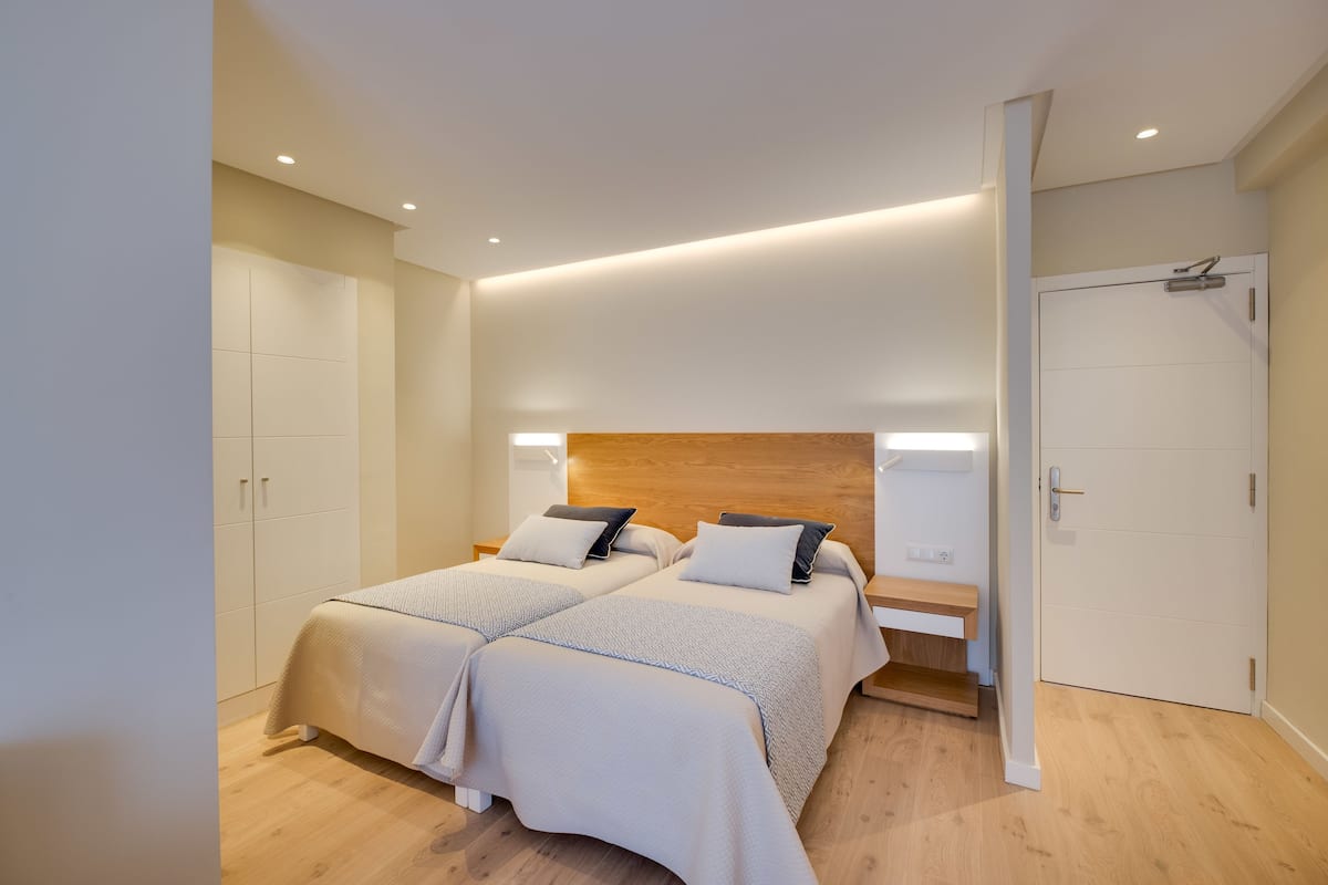 A modern bedroom with two beds, a wooden headboard, and built-in shelving.