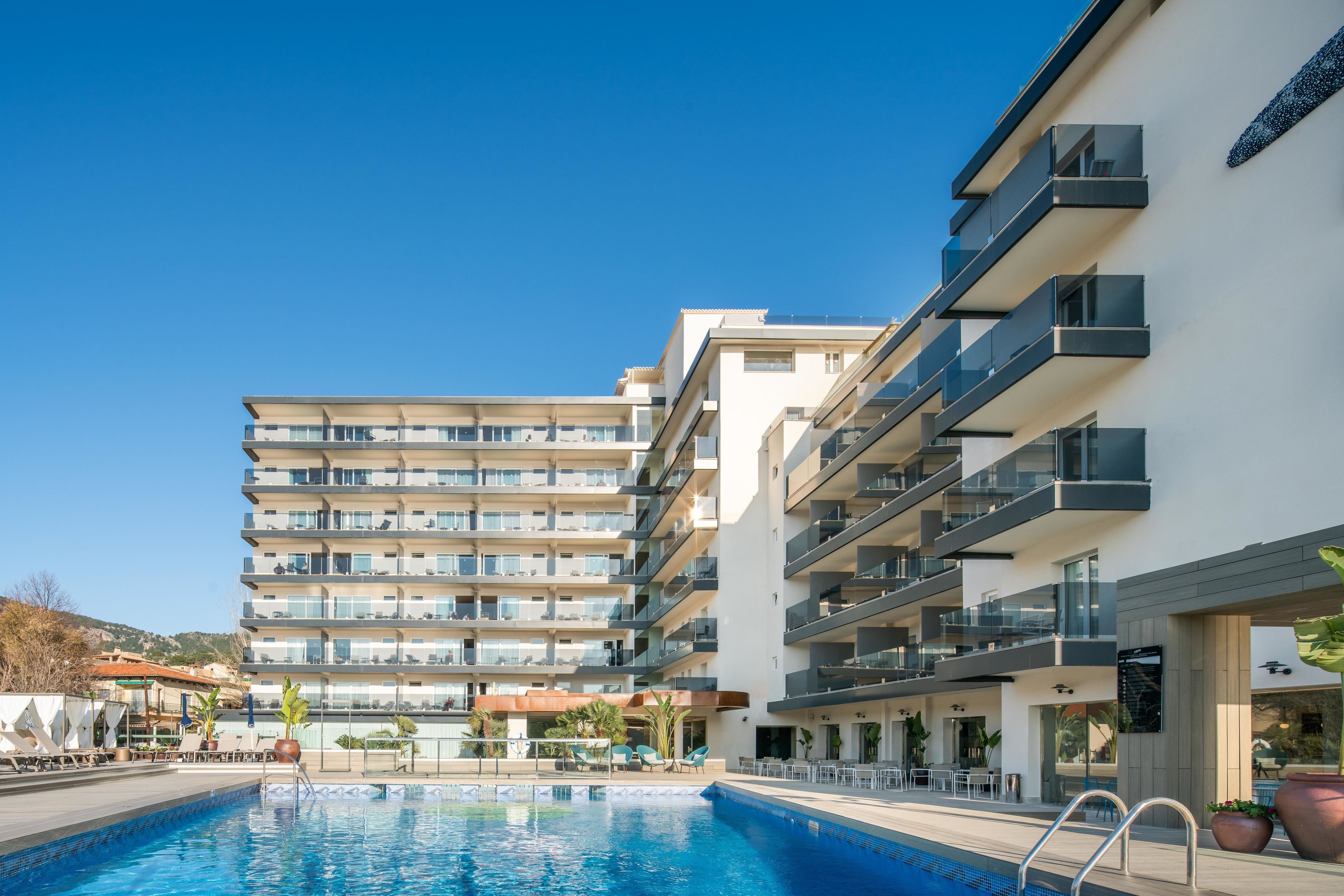 Un hotel moderno con piscina, varios balcones y zonas de estar al aire libre.