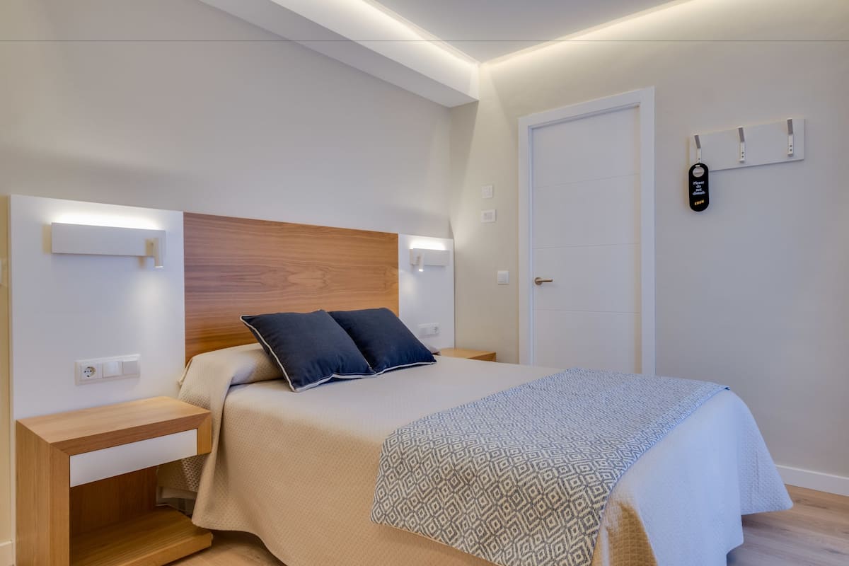 A modern bedroom with a wooden headboard, two bedside tables, a bed with patterned bedding, and a bedside lamp.