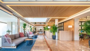 A spacious lobby with a modern design, featuring a reception desk, seating areas, and potted plants.