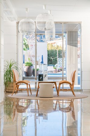 A modern interior with a reflective floor, wicker chairs, a round table, and white pendant lights.