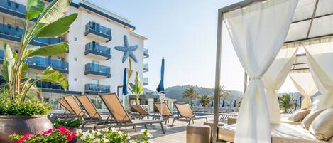 A rooftop pool area with lounge chairs, potted plants, and a canopy bed.