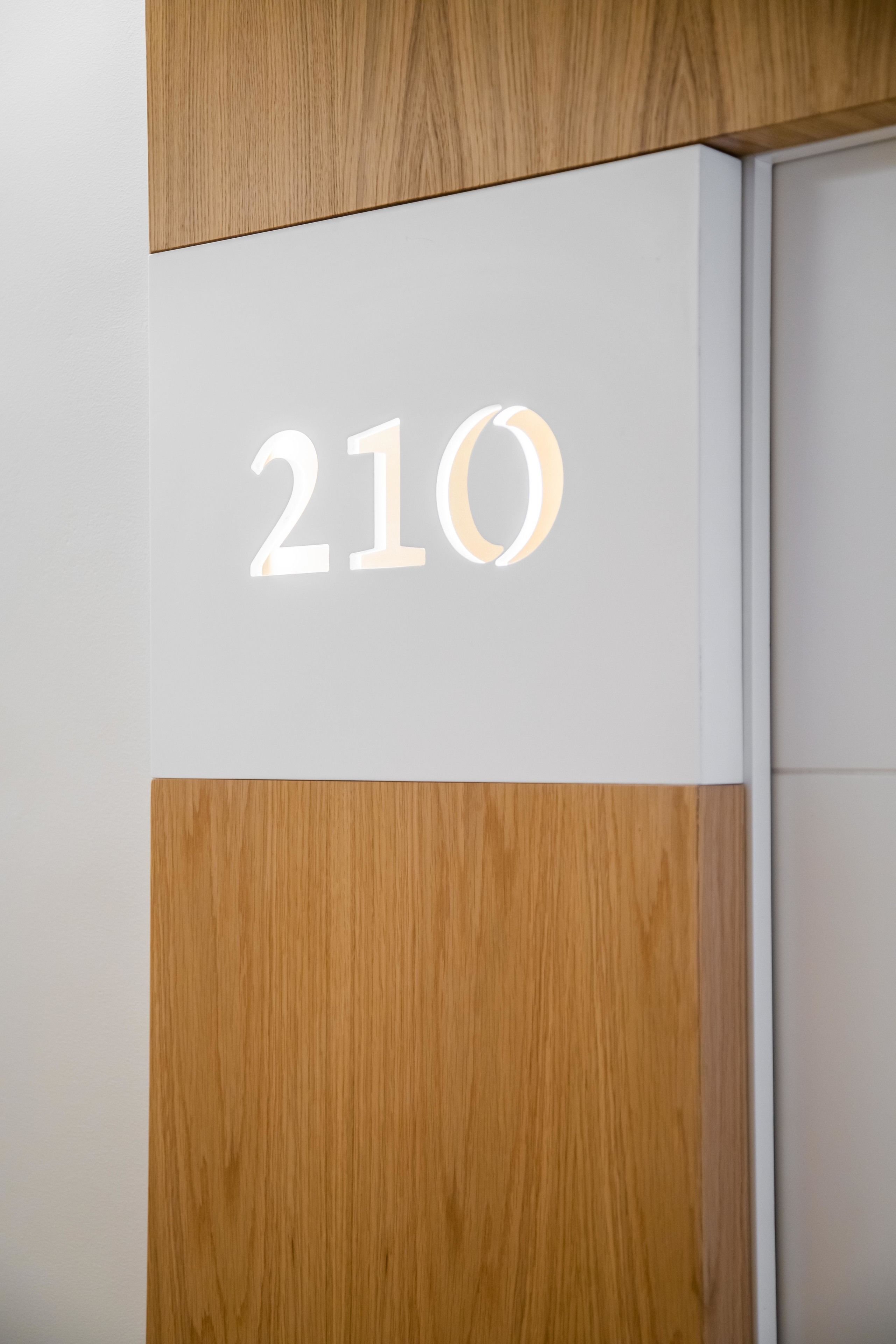 A room number '210' on a wall with a wooden panel design.