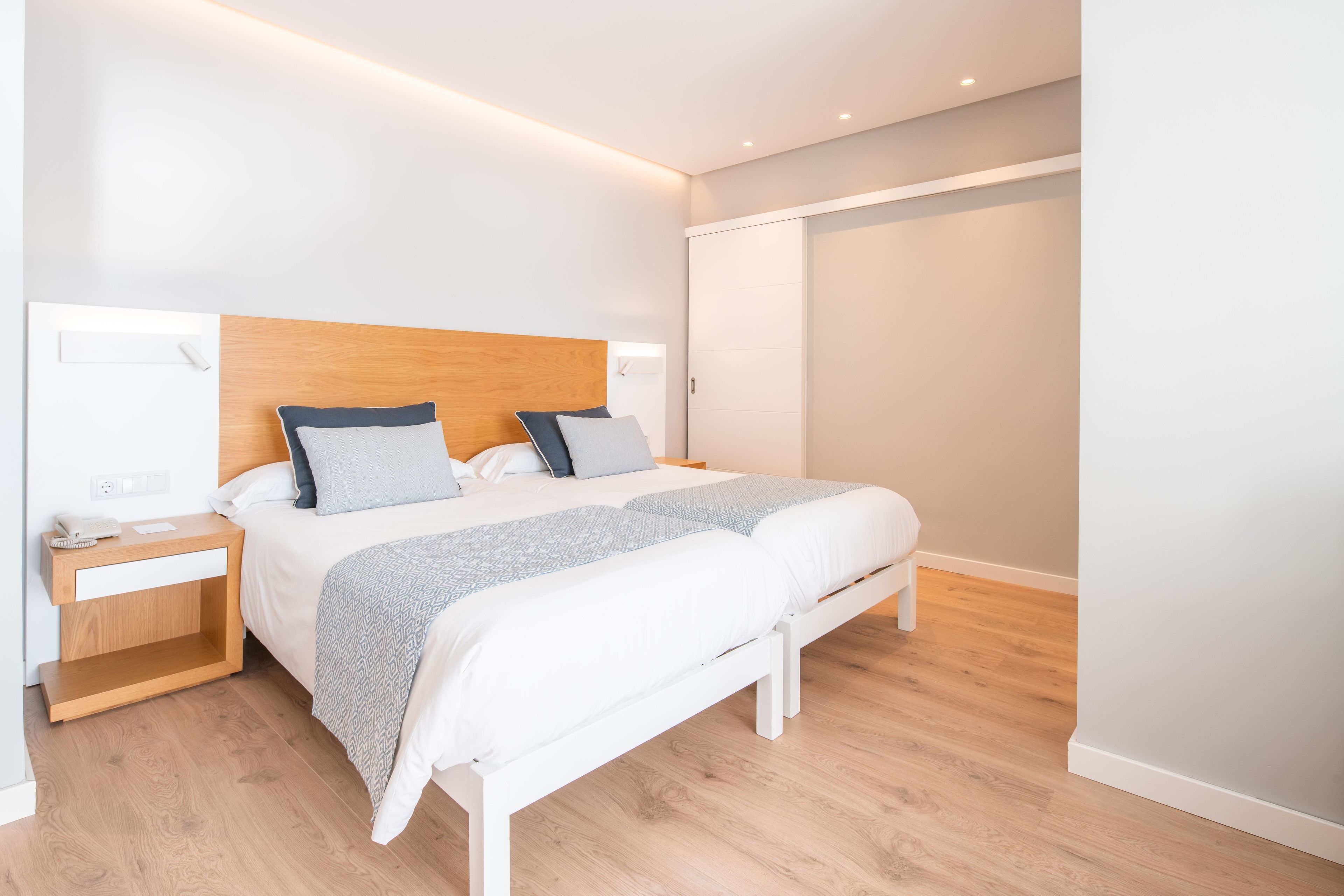 Una camera da letto moderna con una testiera in legno, un letto bianco e un comodino con una lampada.