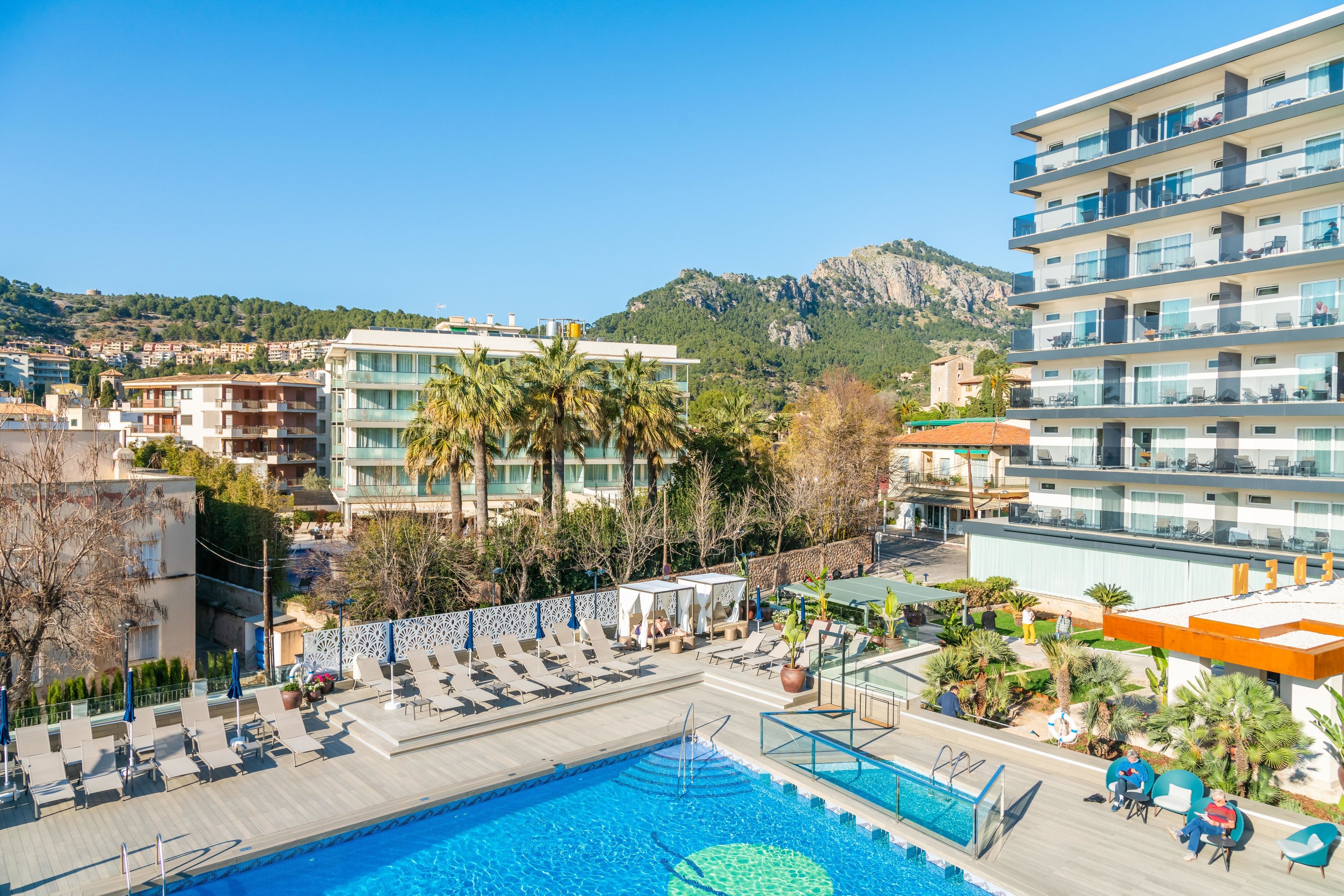 A hotel with a pool area, lounge chairs, and a view of the surrounding buildings and mountains.