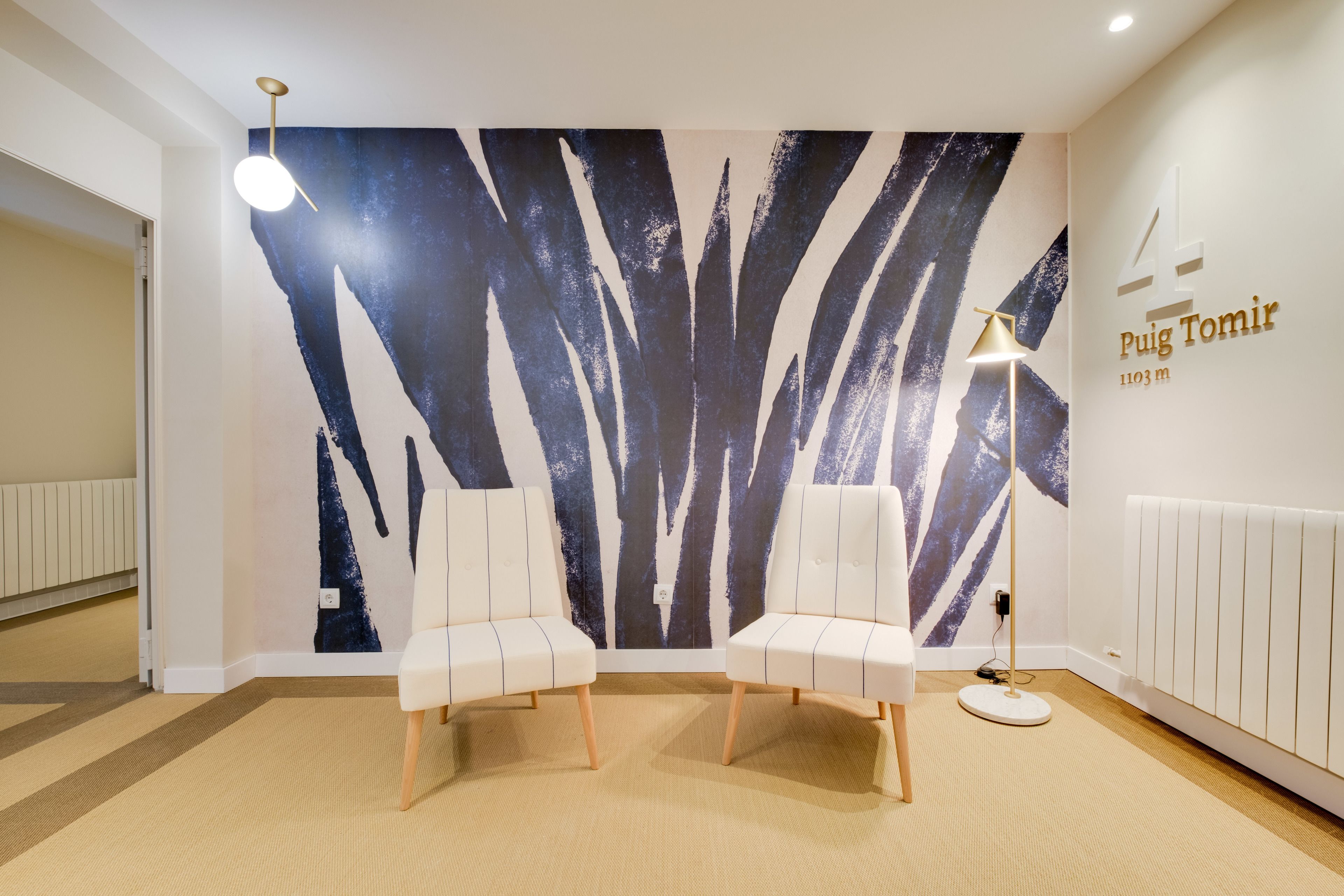 A modern room with two white chairs, a large abstract wall painting, a floor lamp, and a sign indicating the room number and floor.