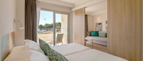 A hotel room with a large bed, a balcony with a view, a sofa, and a wooden wardrobe.