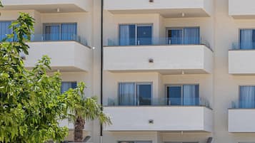 Un hotel de varios pisos con balcones, un cartel que indica que es el Js Portocolom Suites Hotel, y una palmera en primer plano.