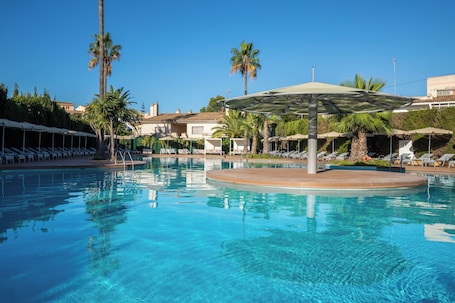 Una piscina al aire libre, sombrillas, sillones reclinables de piscina