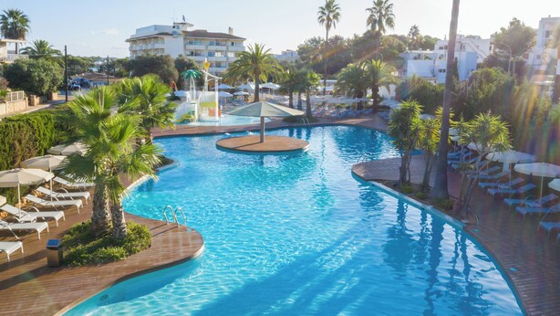 A resort pool area with lounge chairs, palm trees, and a clear blue pool. - Hotel JS PortoColom Suites (Felanitx)