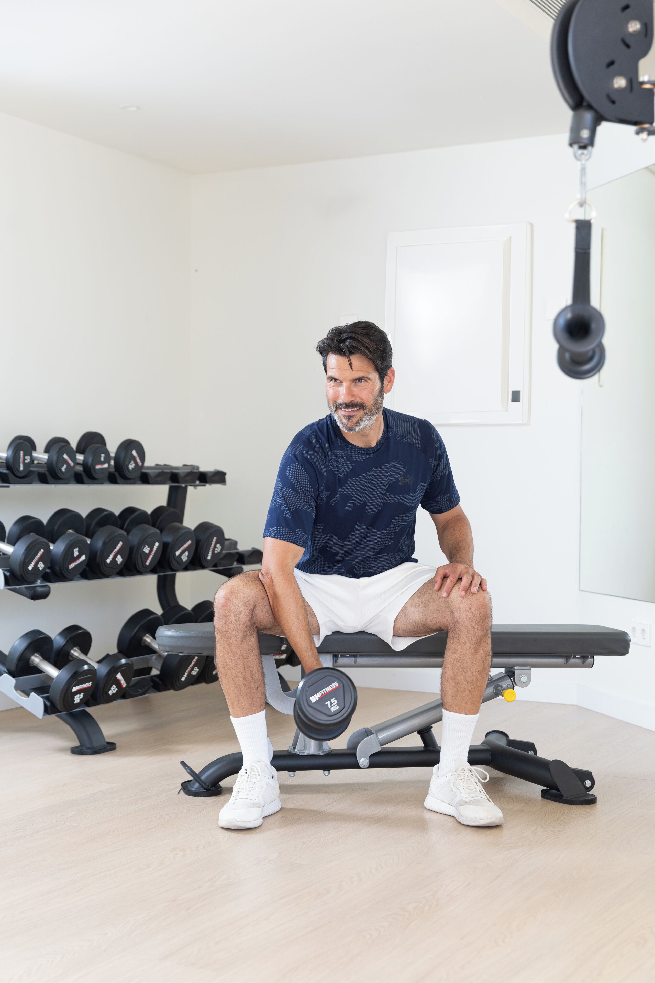 A man sitting on a bench in a gym with weightlifting equipment in the background.