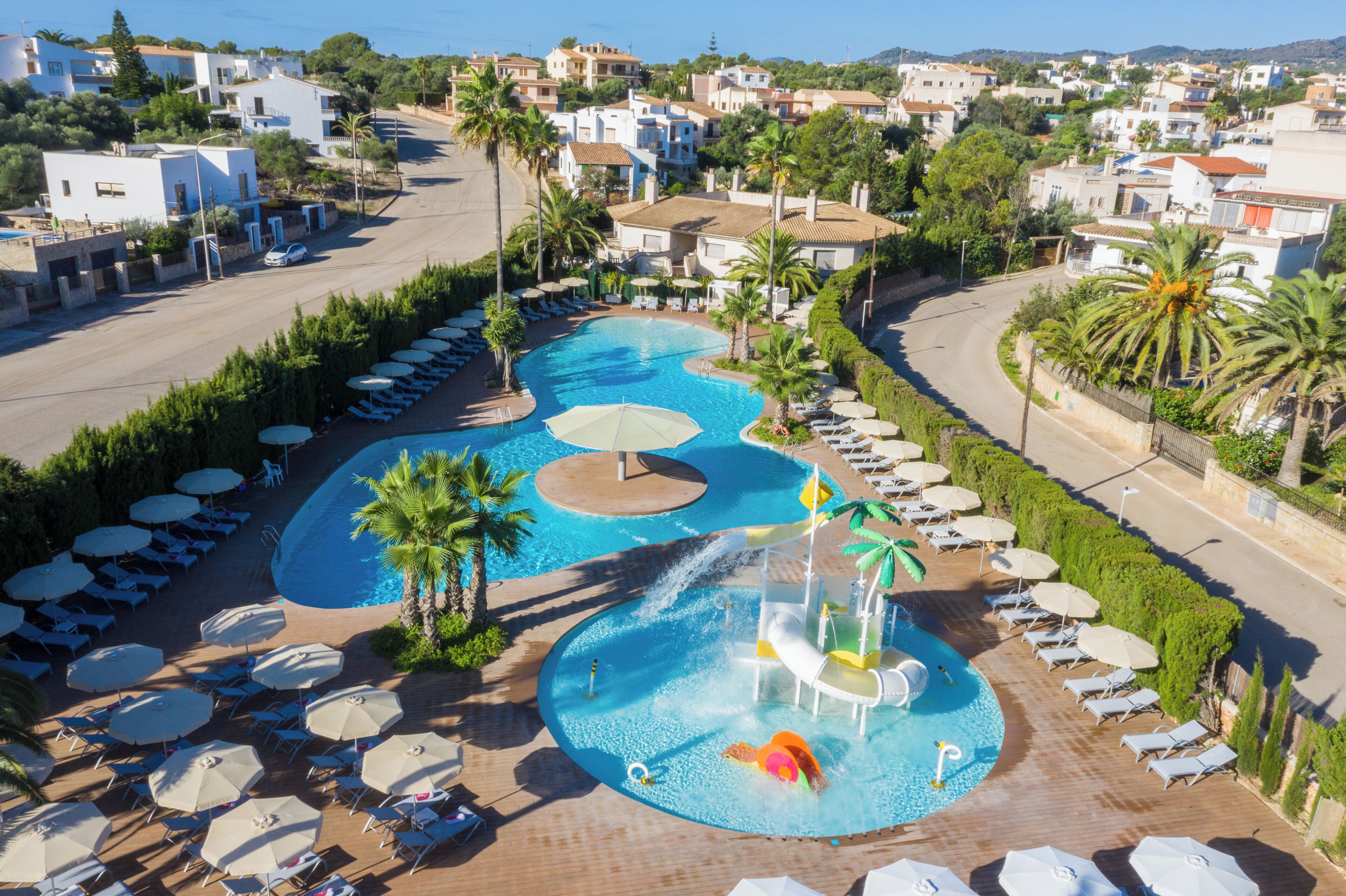 A resort with a large swimming pool, sun loungers, and a water slide.