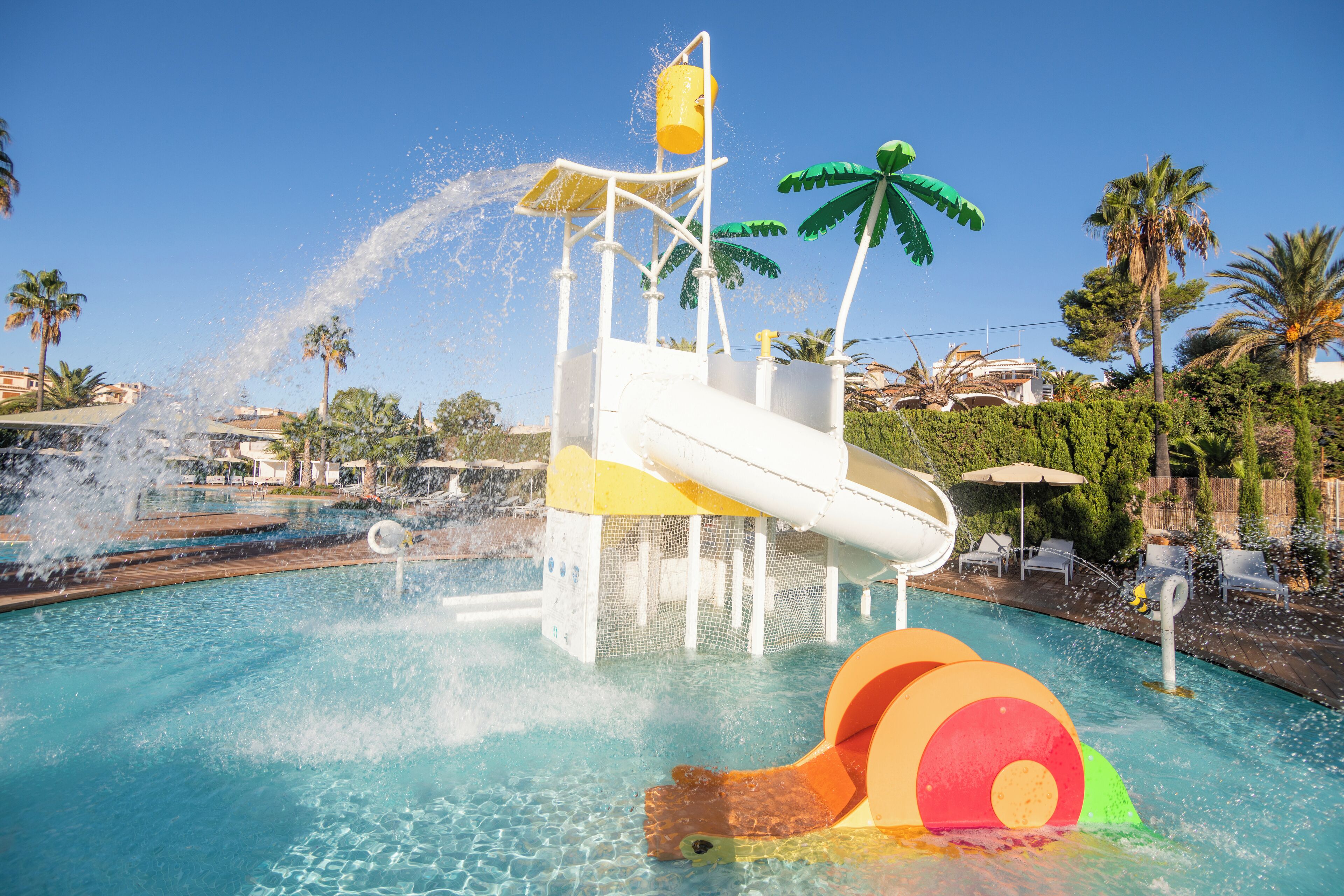 A water park with a water slide, palm trees, and a pool.