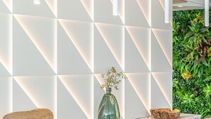 A modern reception area with a geometric wall design, a marble reception desk, and a green wall with plants. - Hotel JS PortoColom Suites (Felanitx)
