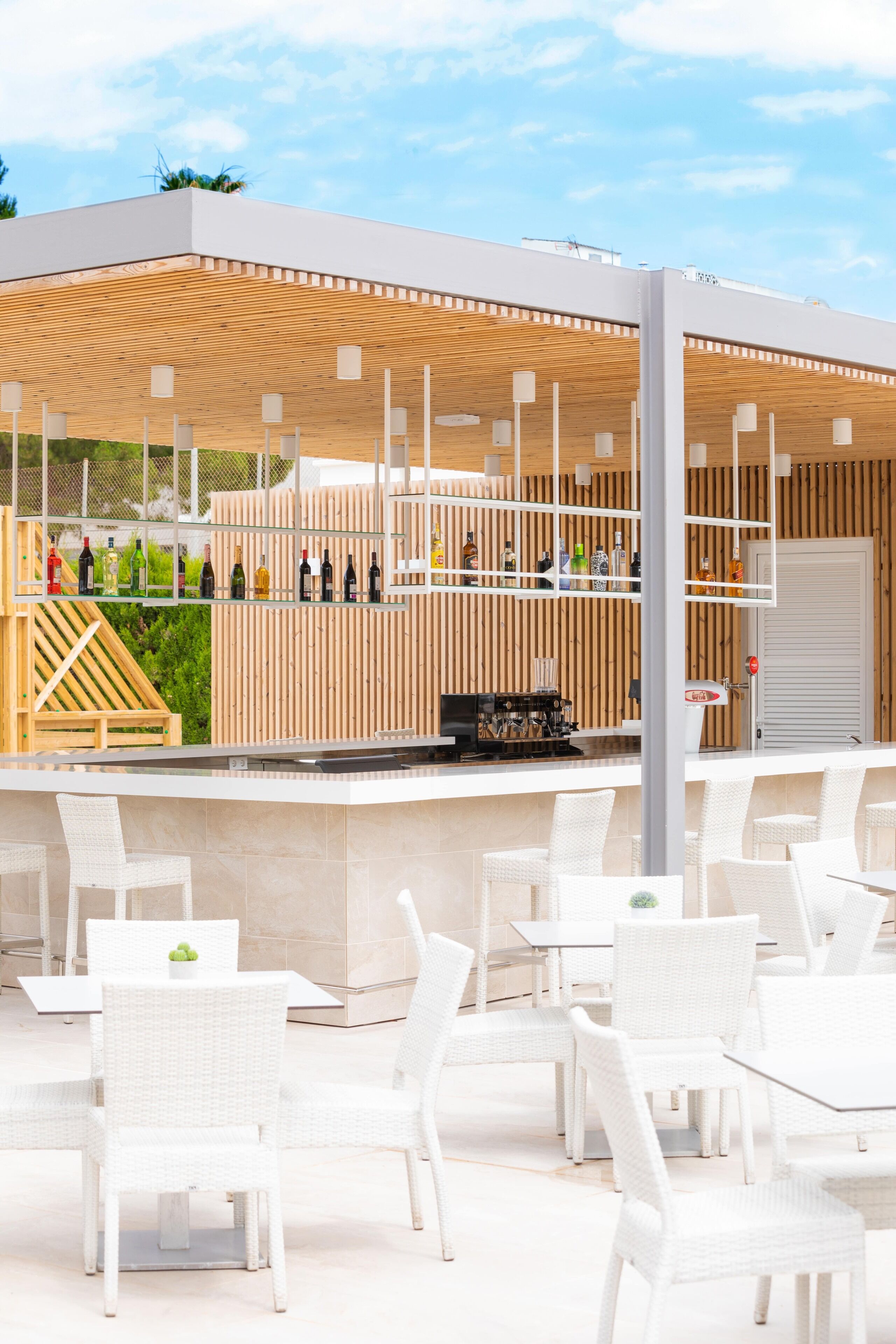 Un área de bar exterior moderna con mobiliario de ratán blanco y techo de listones de madera.