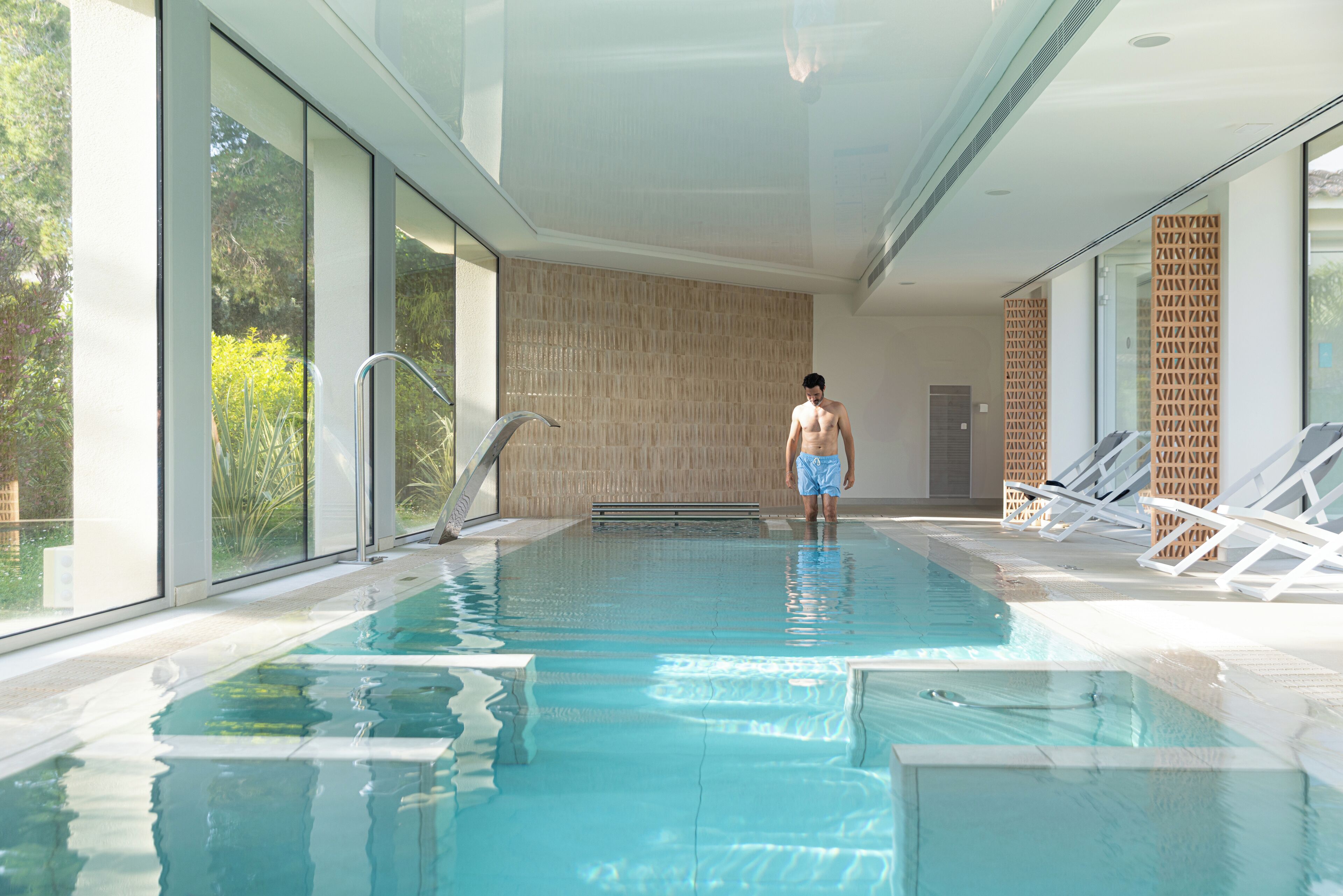 Une piscine à l’eau claire, avec un sol carrelé, et une personne debout au fond.