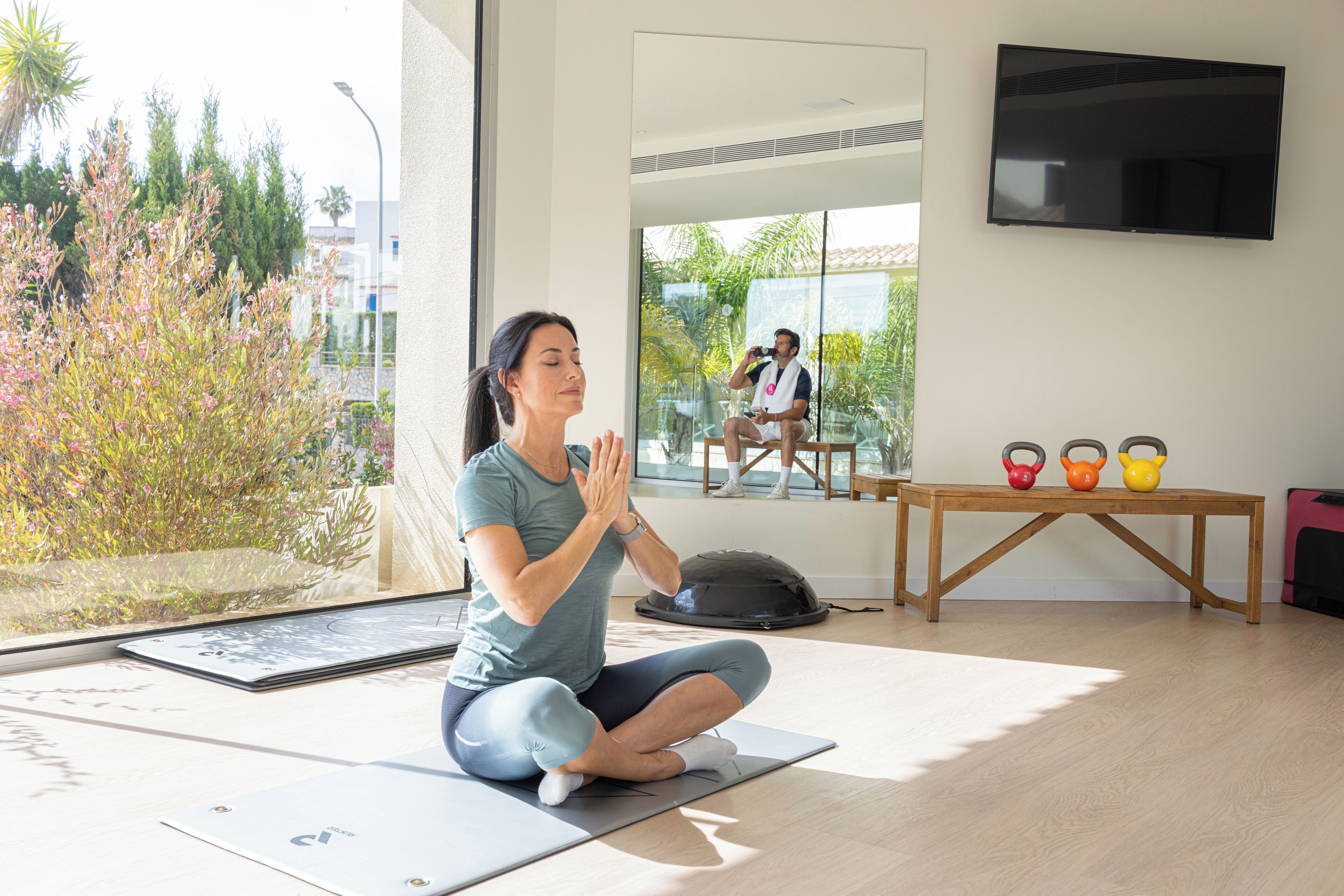 A yoga mat on the floor, a table with kettlebells, and a TV on the wall.