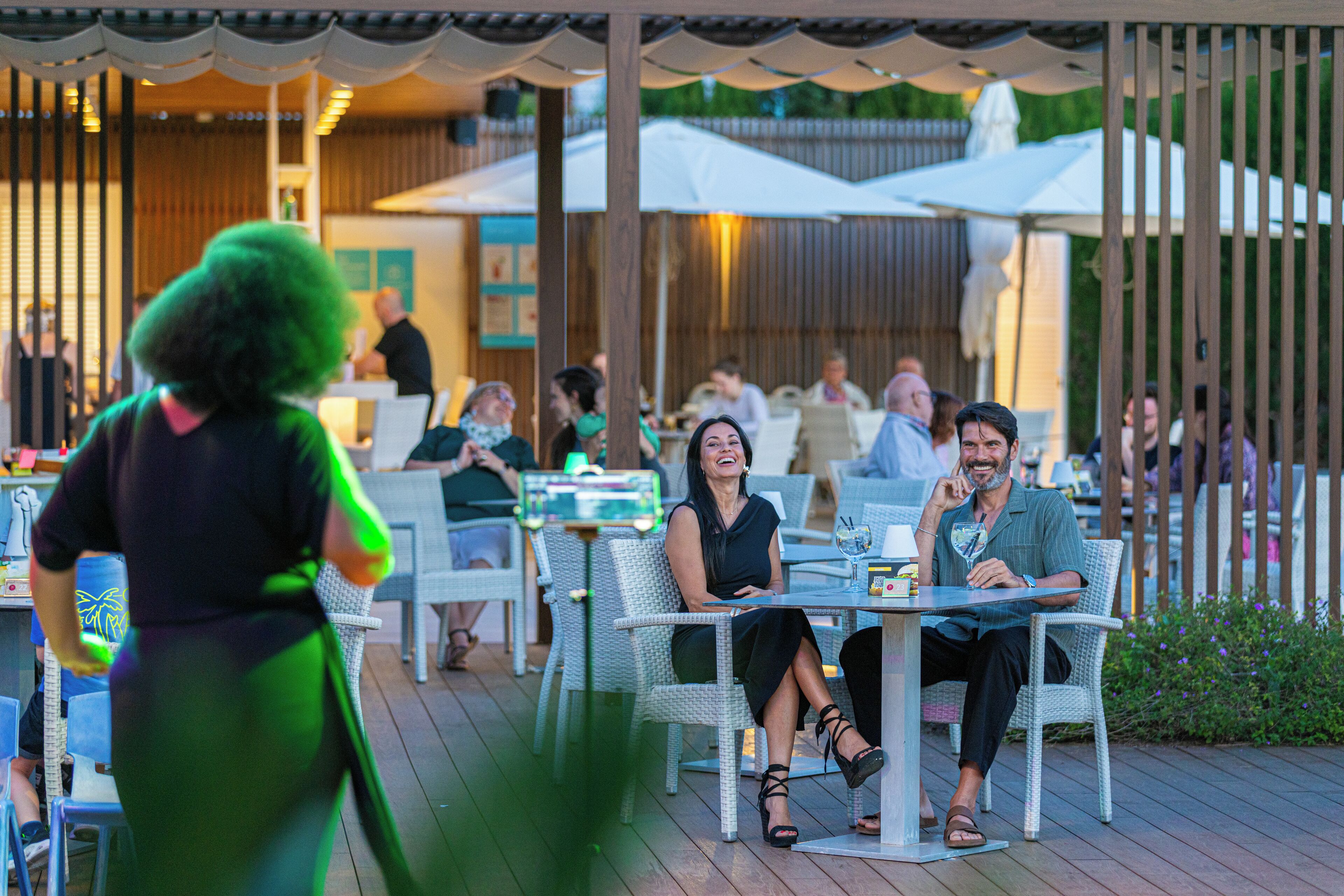 An outdoor dining area with wicker chairs and tables, surrounded by umbrellas and a wooden fence.