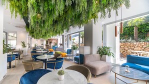 A modern lounge area with round tables, blue and beige chairs, and hanging greenery. - Hotel JS PortoColom Suites (Felanitx)
