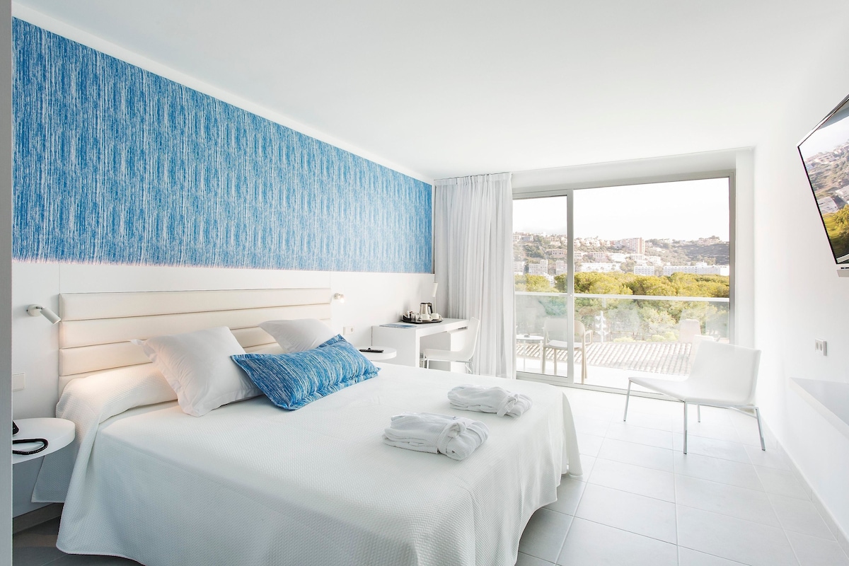 Une chambre d’hôtel avec un lit, un bureau, une chaise et un balcon donnant sur la ville.
