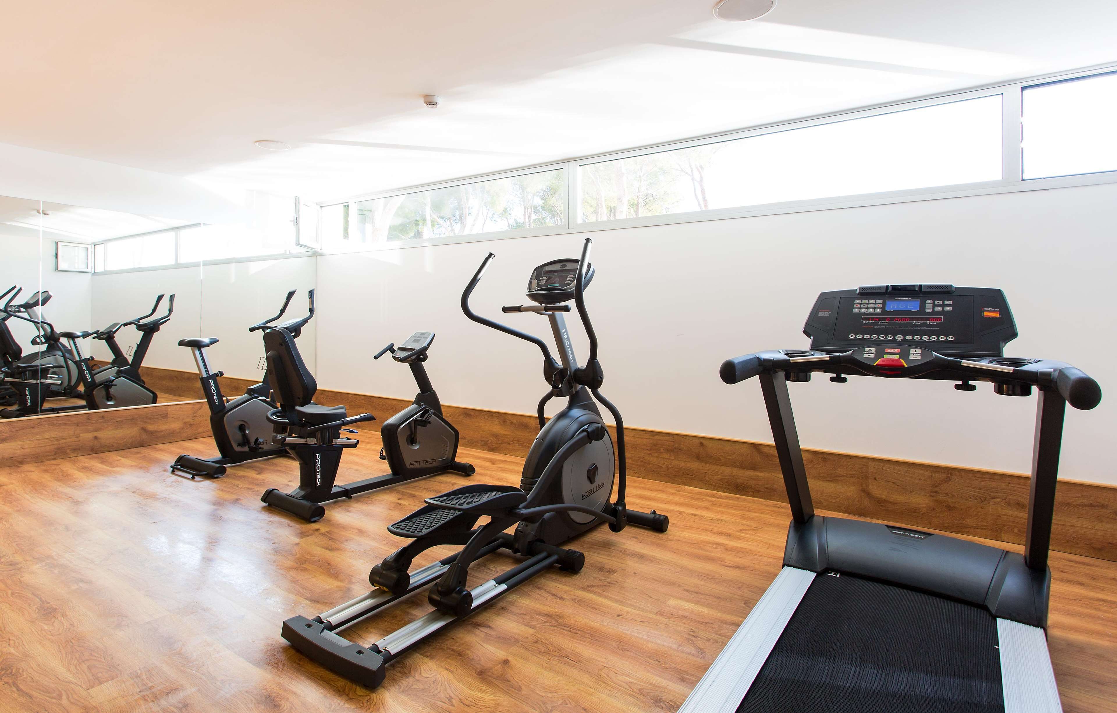 Une salle de sport équipée de divers appareils d’exercice, notamment des tapis de course et des vélos d’appartement, dans une pièce dotée de grandes fenêtres et d’un plancher en bois.