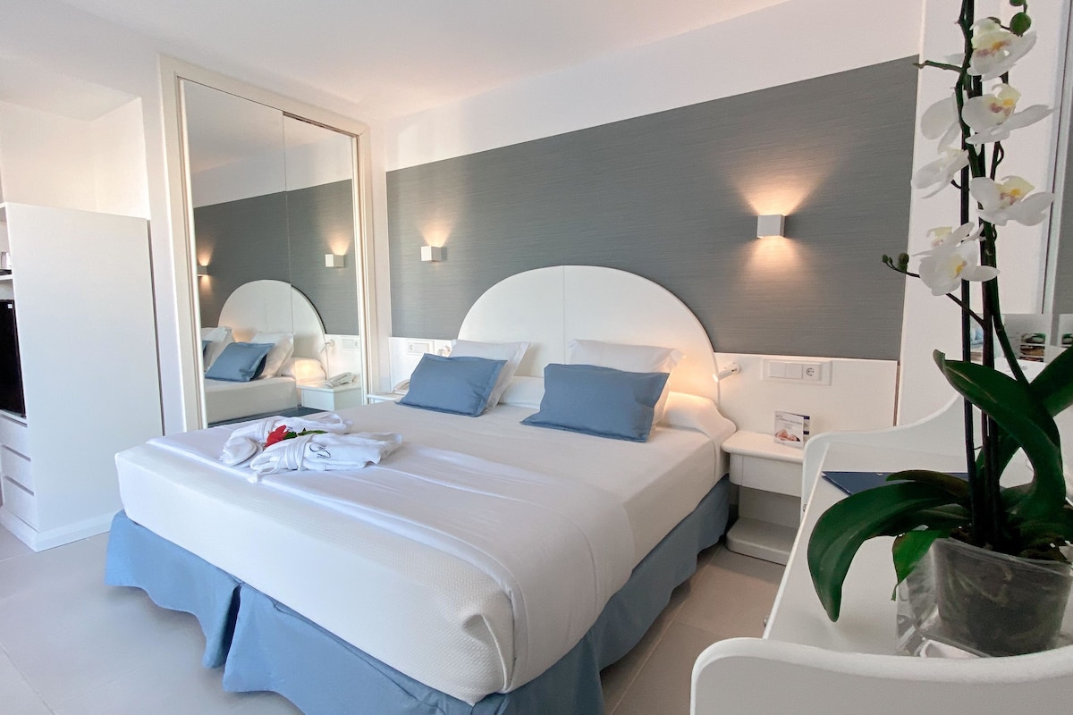 Une chambre d’hôtel avec un lit, des tables de chevet, un miroir, une plante en pot et une armoire.