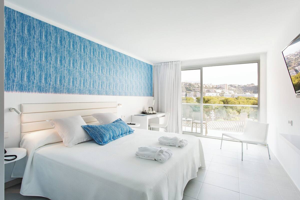 Habitación de hotel con cama, escritorio, silla y balcón con vista a la ciudad.