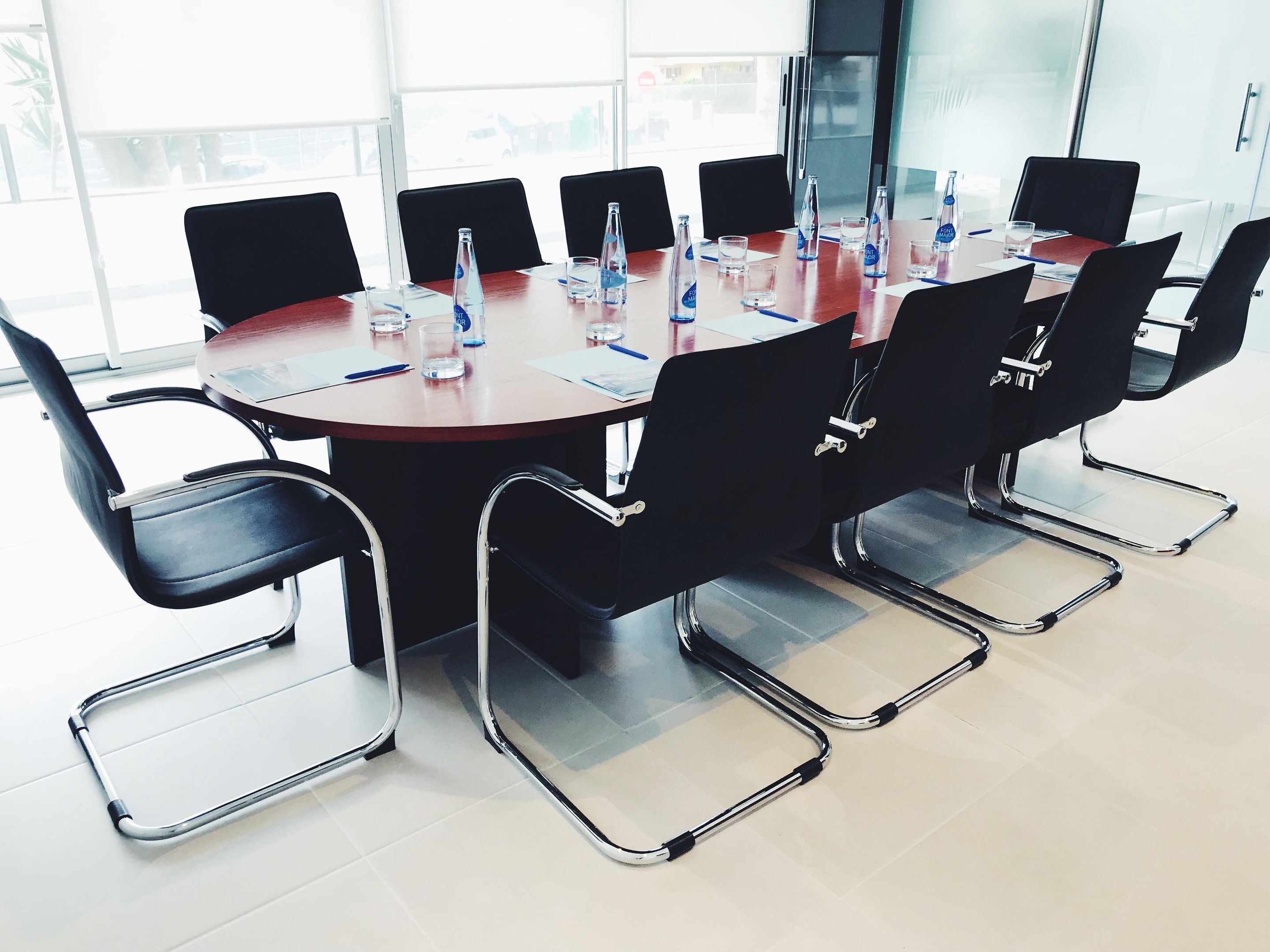 Un salón de conferencias con una mesa redonda, sillas negras y botellas de agua.